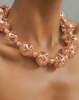 Close-up of sculptural rose gold necklace featuring alternating large openwork globes and petite textured beads.