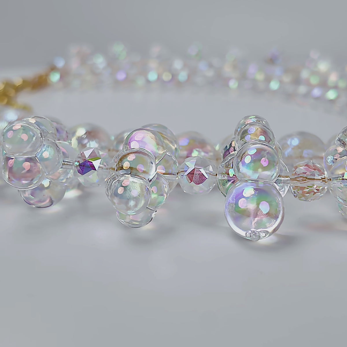Close up of layered iridescent statement necklace with clustered bubble beads and a delicate faceted center strand.