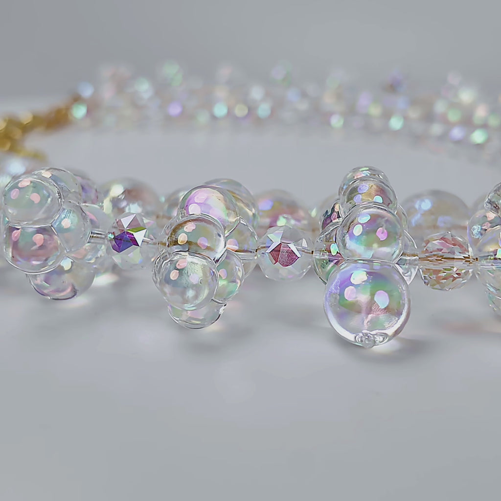 Close up of layered iridescent statement necklace with clustered bubble beads and a delicate faceted center strand.
