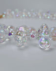 Close up of layered iridescent statement necklace with clustered bubble beads and a delicate faceted center strand.