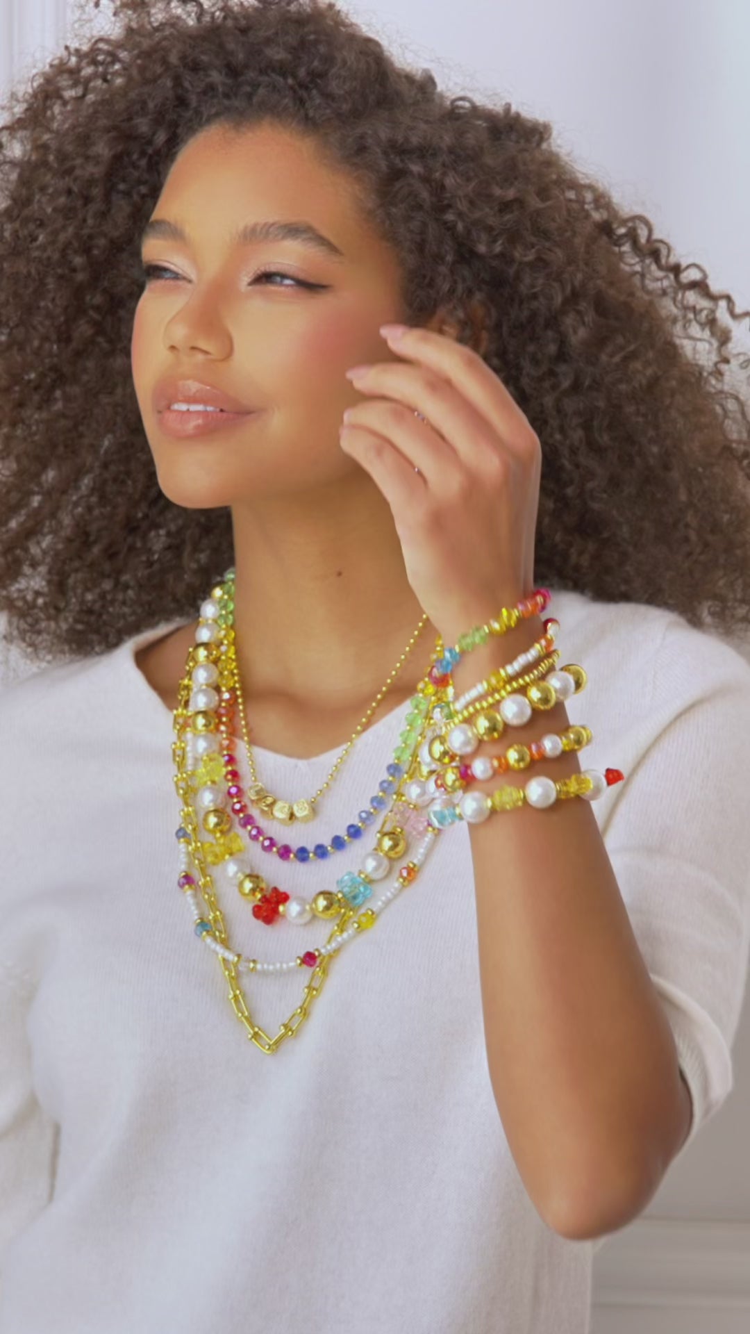 Stacked pearl and colorful bead stretch bracelets with gold accents and playful charms designed for layered wrist styling