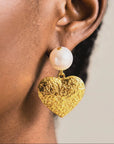 Romantic statement dangle earrings featuring ivory pearls and polished gold hearts with raised decorative texture.