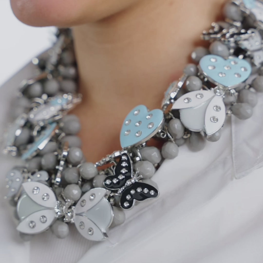 Sassy Jones Lovebug Greige Bib featuring whimsical dimensional motifs in powder blue, soft gray, black and neutral tones.