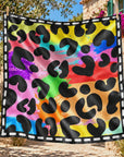close up of A square scarf with a vibrant rainbow watercolor splatter background and black leopard spots, finished with a white dashed border, shown on a light gray background.