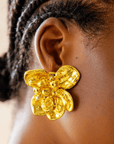 18k gold sculptural floral statement earrings inspired by wisteria blossoms with layered petals and faceted gold center worn on a woman’s ear