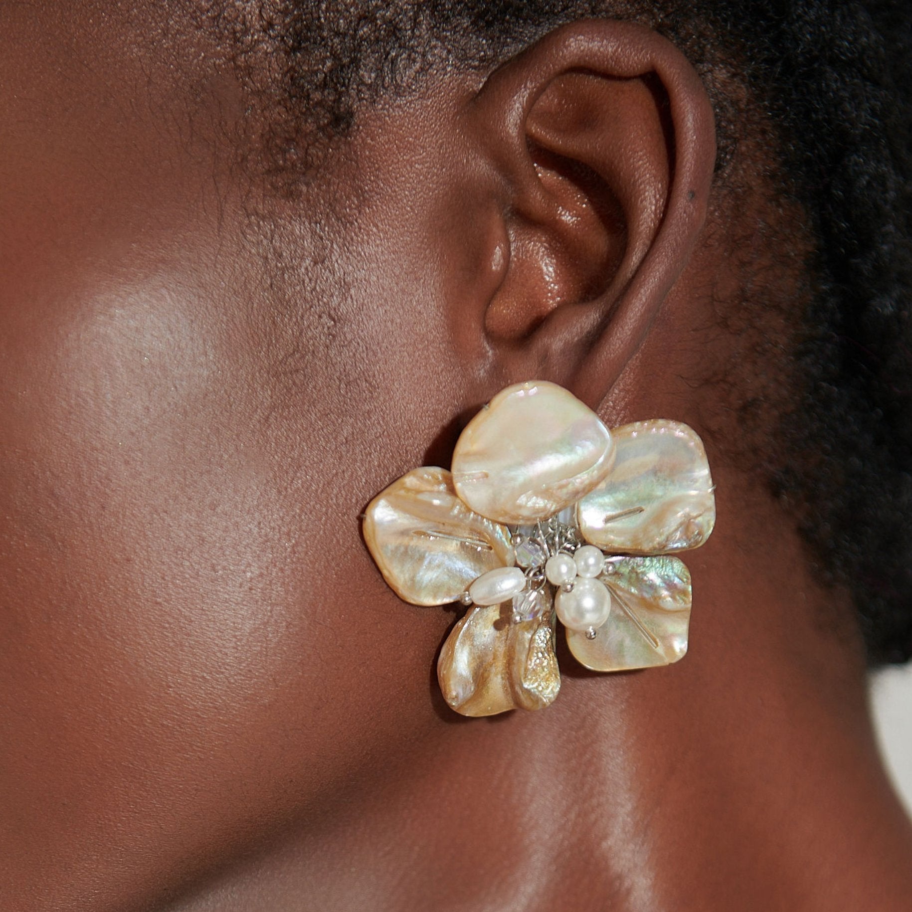 Mother of pearl floral statement earrings with pearl cluster center inspired by wisteria blossoms worn on a woman's ear